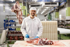 A butcher is cutting raw meat into pieces while smiling at the camera.